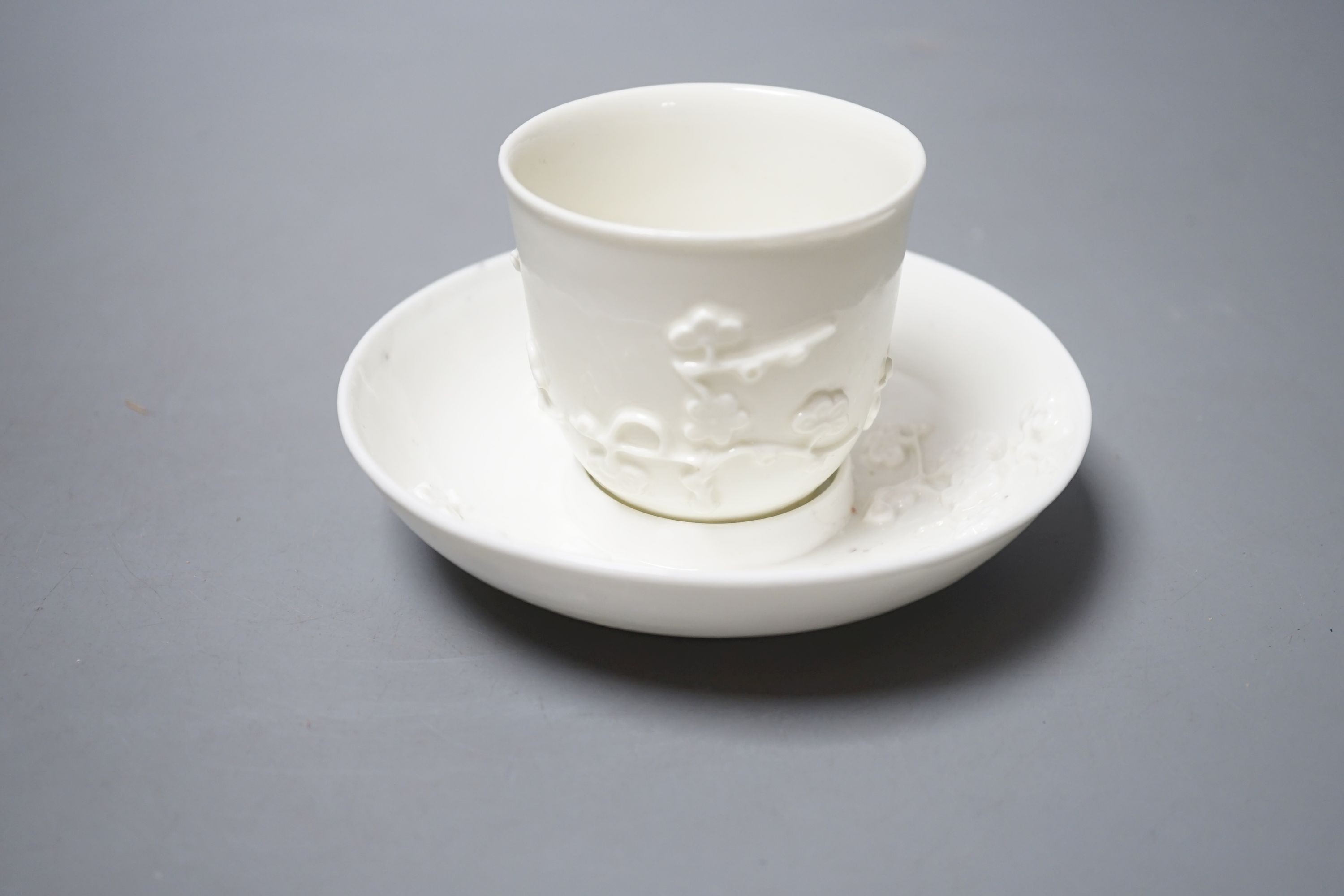 A St Cloud white-glazed coffee cup with angular handle and scroll terminal and matching trembleuse saucer applied with sprigs of flowering prunus c. 1730